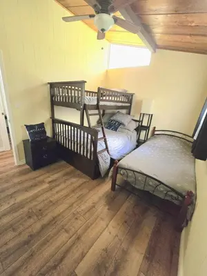 two beds in a room with wood floors and a ceiling at Lovely Little Lake House in Brighton