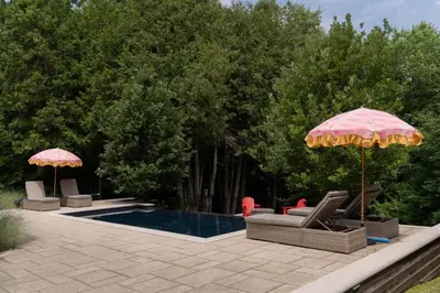 a pool with two umbrellas and lounge chairs and a swimming pool at Cozy Private Suite with Year-Round Hot Tub in Elora
