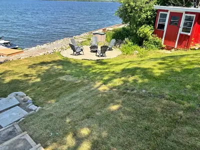 a yard with chairs and a red shed next to the water at Rice Lake Retreat in Roseneath