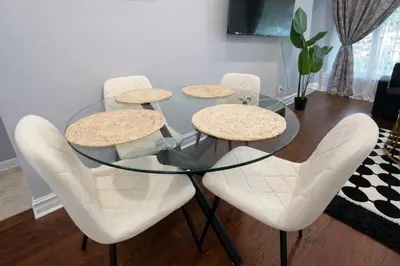 a glass table with four white chairs around it at Newly Renovated 3BR North York Bungalow with Backyard Patio & Volleyball Set! Close to Rogers Stadium, TTC Subway Access, Perfect for Family Travel, Group Trips & Work Stays! in Toronto