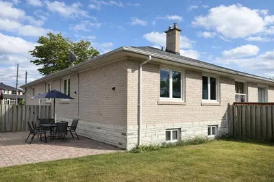 a white brick house with a table and chairs at Newly Renovated 3BR North York Bungalow with Backyard Patio & Volleyball Set! Close to Rogers Stadium, TTC Subway Access, Perfect for Family Travel, Group Trips & Work Stays! in Toronto