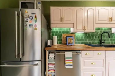 a kitchen with white cabinets and a stainless steel refrigerator at The Parkdale Cottage in Toronto