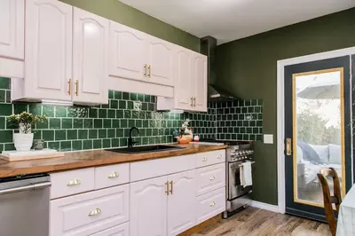 a kitchen with white cabinets and green tiles at The Parkdale Cottage in Toronto