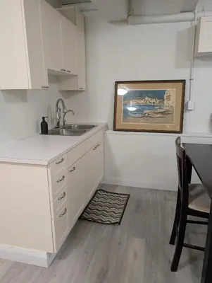 a kitchen with white cabinets and a sink and a table at Cozy Bachelor Unit in Guelph