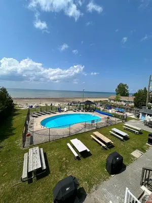 a pool with benches and umbrellas next to the beach at The Driftwood Deck in Wasaga Beach