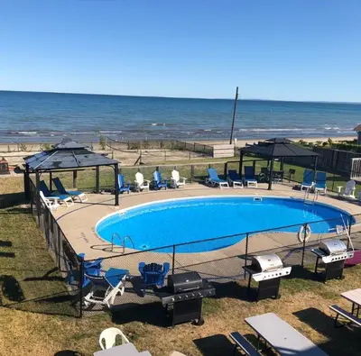 a swimming pool with chairs and umbrellas next to the ocean at The Driftwood Deck 5B in Wasaga Beach