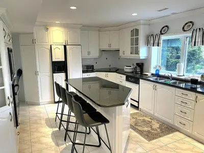 a kitchen with white cabinets and a island with bar stools at Summer Escape Close to the City in Newmarket