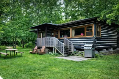 a log cabin with a porch and a table and benches at 2-Bedroom - Balsam Lake Cottages Resort #12 in Kawartha Lakes