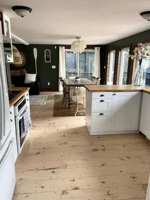 a kitchen with white cabinets and a dining room with a table at Muskoka Cabana - Sandy beach cottage in Muskoka in Utterson
