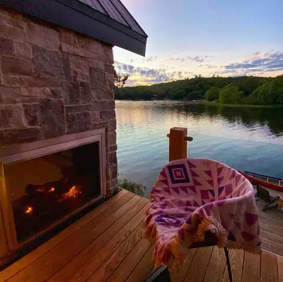 a fireplace sitting on a deck next to a lake at The Water’s Edge * * Unique Muskoka Treehouse * * in Utterson