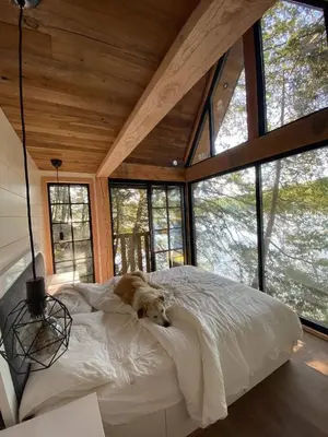 a dog laying on a bed in a room with windows at The Water’s Edge * * Unique Muskoka Treehouse * * in Utterson