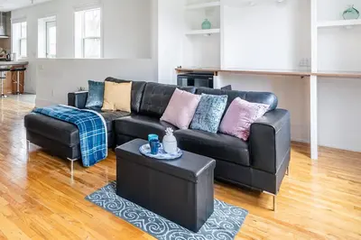 a living room with a black leather couch and a table at Stylish & Pet-Friendly 2BR Suite in Trendy Leslieville with Portable AC Nearest Intersection Eastern Ave in Toronto