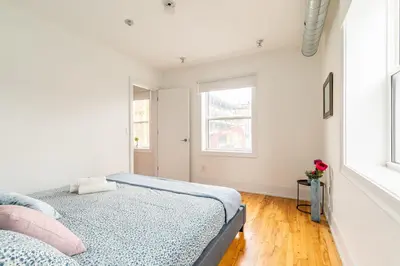 a white bedroom with a bed and two windows at Stylish & Pet-Friendly 2BR Suite in Trendy Leslieville with Portable AC Nearest Intersection Eastern Ave in Toronto