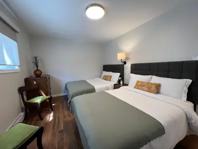 a bedroom with two beds and a chair and a window at Spacious Ground Floor Garden View Apartment in Wasaga Beach