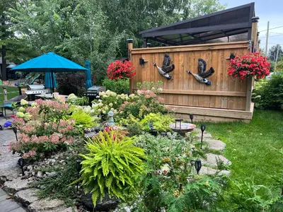 a garden with flowers and a fence with birds on it at The Cozy Shore Cottage - Large in Wasaga Beach