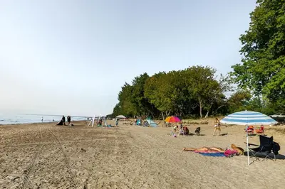 a group of people on a beach with umbrellas at The Cozy Shore Cottage - Standard Attached in Wasaga Beach