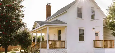 a white house with a porch and a tree at The Wild Rose - Cozy PEC Rental in Picton in Picton