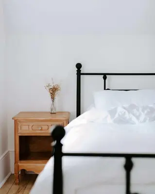 a bed with white sheets and a nightstand with a vase on it at The Wild Rose - Cozy PEC Rental in Picton in Picton