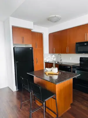 a kitchen with a black refrigerator and wooden cabinets at Modern One Bedroom Near Square One With Free Parking in Mississauga
