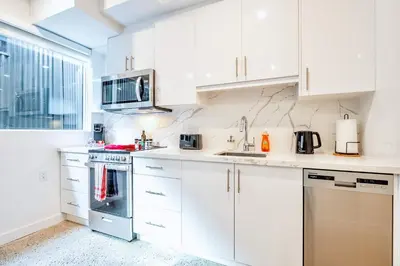 a white kitchen with white cabinets and appliances at Inviting 2BR Basement Suite in Downtown Toronto - The Roland in Toronto