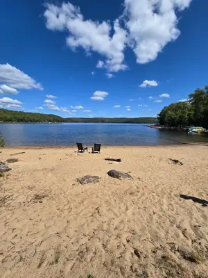 two chairs sitting on a sandy beach next to a lake at The Beaver Den in Haliburton