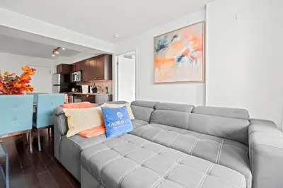 a living room with a gray couch and a kitchen at Autumnaly Whisper 2 BR & DEN in the Heart of the City in Toronto