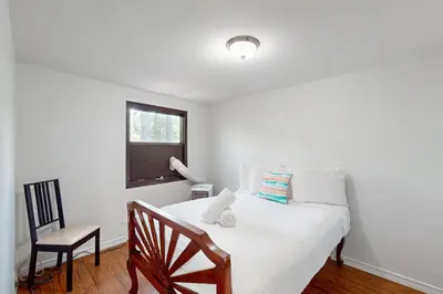 a bedroom with a white bed with a chair and a window at Lazy Daze (House 2) in Wasaga Beach