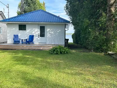 a white cottage with two blue chairs on a deck at Water Front Cottage - Balsam Lake in Victoria Road