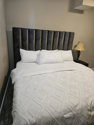 a large bed with a black headboard and white pillows at Beautiful 3 bedrooms, 2 bathrooms, 4 beds sleep 8, basement close to Falls in Niagara Falls