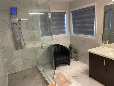 a bathroom with a glass shower with a black chair at Grandeur Homes in Whitby