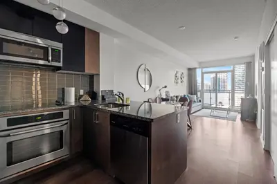 a kitchen with stainless steel appliances and a living room at Modern 1Bd & Den Condo with Balcony Lillian St in Toronto