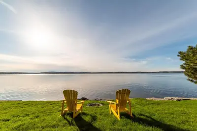 two yellow chairs sitting on the grass near a lake at Luxurious Lakefront Cottage, Sleeps 12 in Bewdley