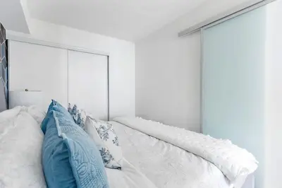 a white bedroom with blue pillows on a bed at Charming Condo w Private Patio in Quiet Capreol in Toronto