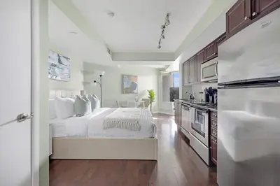 a white bedroom with a bed and a kitchen at Cozy Waterfront Studio plus Parking by the Bentway in Toronto