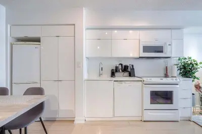 a white kitchen with white appliances and a table at Modern 2 Bedroom plus Den Condo with Balcony Downtown Toronto in Toronto