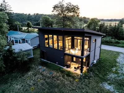 a small black tiny house sitting on top of a field at Casa Luna Chic Lakehouse BBQ Game Room LakeViews in Orillia