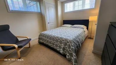 a bedroom with a bed and a chair and two windows at Spacious 2 BR, 3 beds, sleeps 6, kitchen, laundry in Richmond Hill