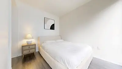 a white bedroom with a bed and a nightstand with a lamp at Cozy 1BR Condo in Core Toronto in Toronto