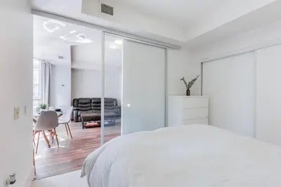 a white bedroom with a bed and a dining room at Modern Down Town Condo Near CN Tower with Fast WiFi in Toronto