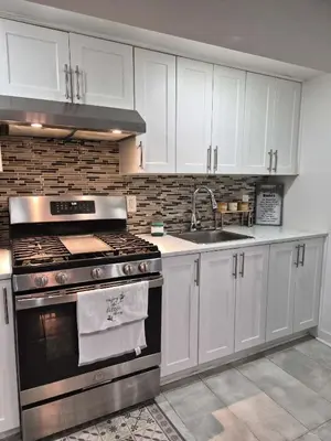 a kitchen with white cabinets and a stove and a sink at Equipped Basement Great Location in London