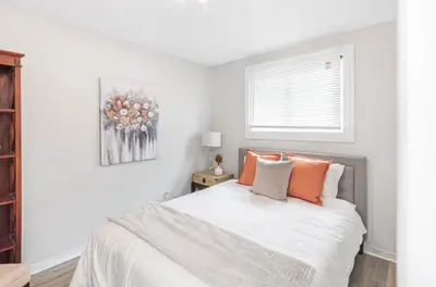 a white bedroom with a bed with orange pillows at Quaint and Stylish UPPER level 3-bed bungalow in Hamilton, ON in Hamilton