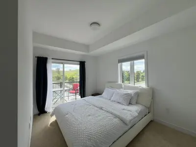 a white bedroom with a bed and a window at Stylish 2-Story Condo with Balcony in Kitchener