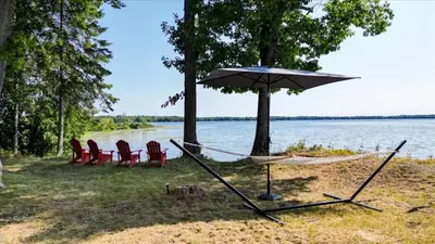 a hammock with chairs and an umbrella next to a lake at Pet friendly- Crystal Water fishing Family Retreat in Havelock