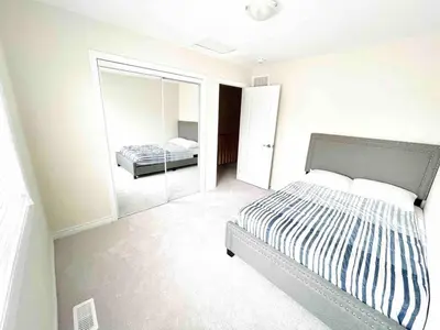 a white bedroom with a bed and a mirror at Two Adjacent Modern Homes in West Niagara Sleep 16 in Thorold