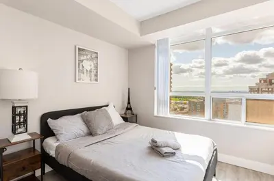 a white bedroom with a bed and a large window at SkyView 2BR Plus Den Stunning Views Steps to SQ1 Mall in Mississauga