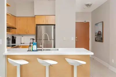 a kitchen with a counter with three white stools at Stylish Fort York Condo w Patio Prime Location in Toronto
