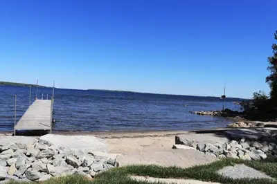 a dock on a beach next to a body of water at Waterfront 3 Bedroom Home in Port McNicoll