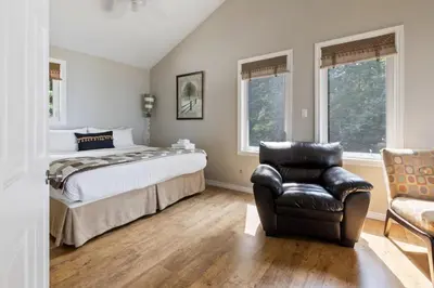 a bedroom with a bed and a leather chair at Serene Waterfront Escape On Private Lane in Thornbury