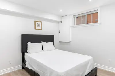 a bedroom with a bed with white sheets and a window at Cozy 3BR 2 Bath Lower Level Close to Shops in Richmond Hill