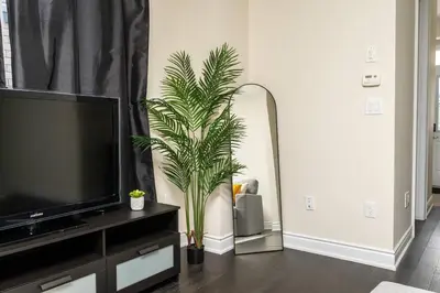 a living room with a tv and a palm plant at Joyful Haven|KingBed|Air Hockey| 10 mins to Falls in Thorold